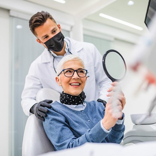 Woman with black glasses smiling at reflection in handheld mirror