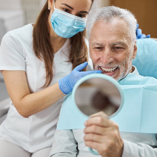 Man with white hair grinning into mirror with dentist touching his teeth