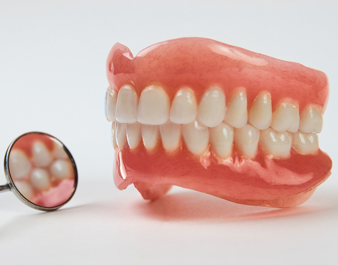 Set of full dentures next to a dental mirror