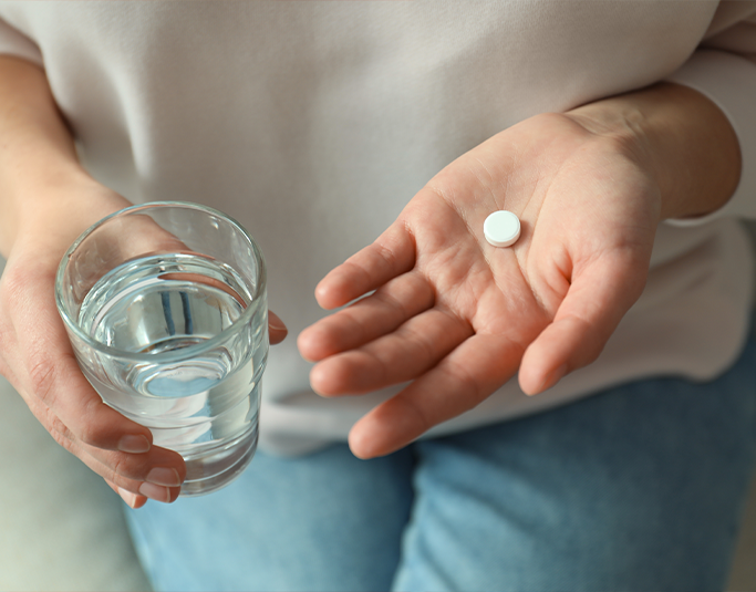 Person holding a white pill and a glass of water