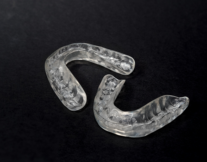 Two clear nightguard trays laying on a black surface