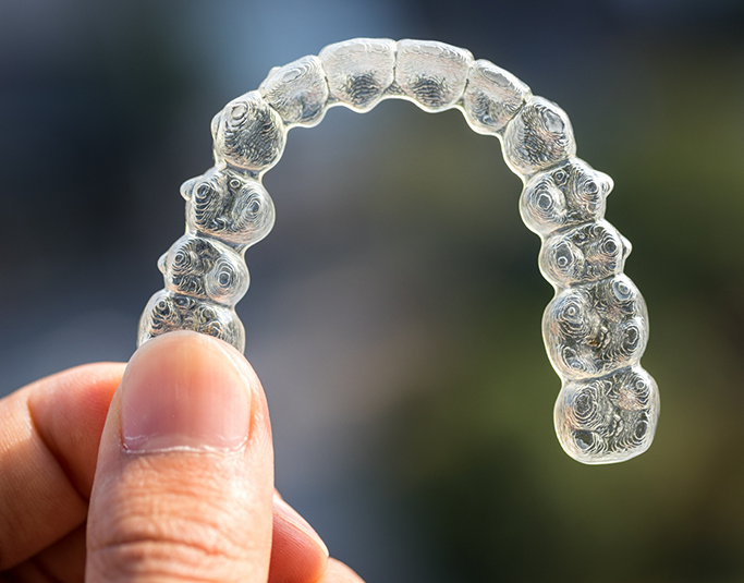 Close up of a hand holding an Invisalign clear aligner
