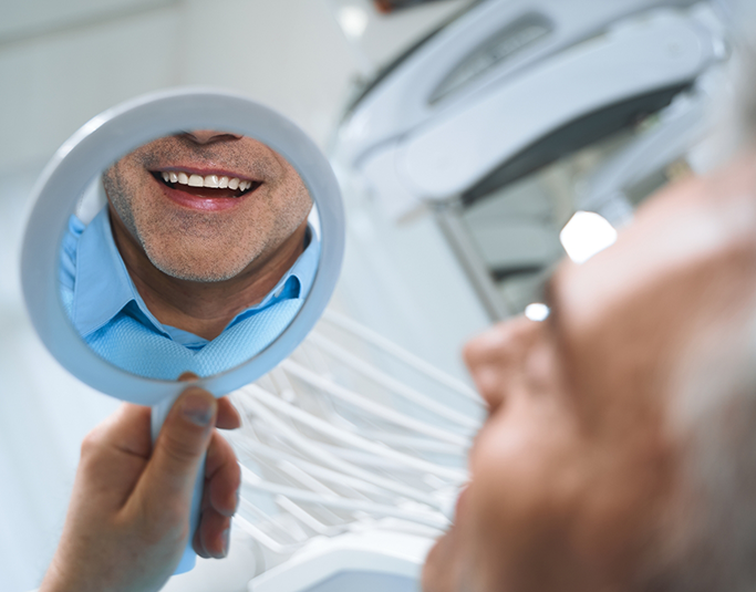 Dental patient looking at his new and improved smile in a mirror