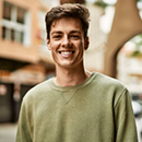 Young man in a green sweater smiling on a city sidewalk
