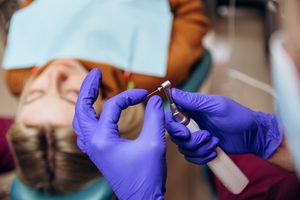 Gloved hands preparing root canal instrument with patient in the background
